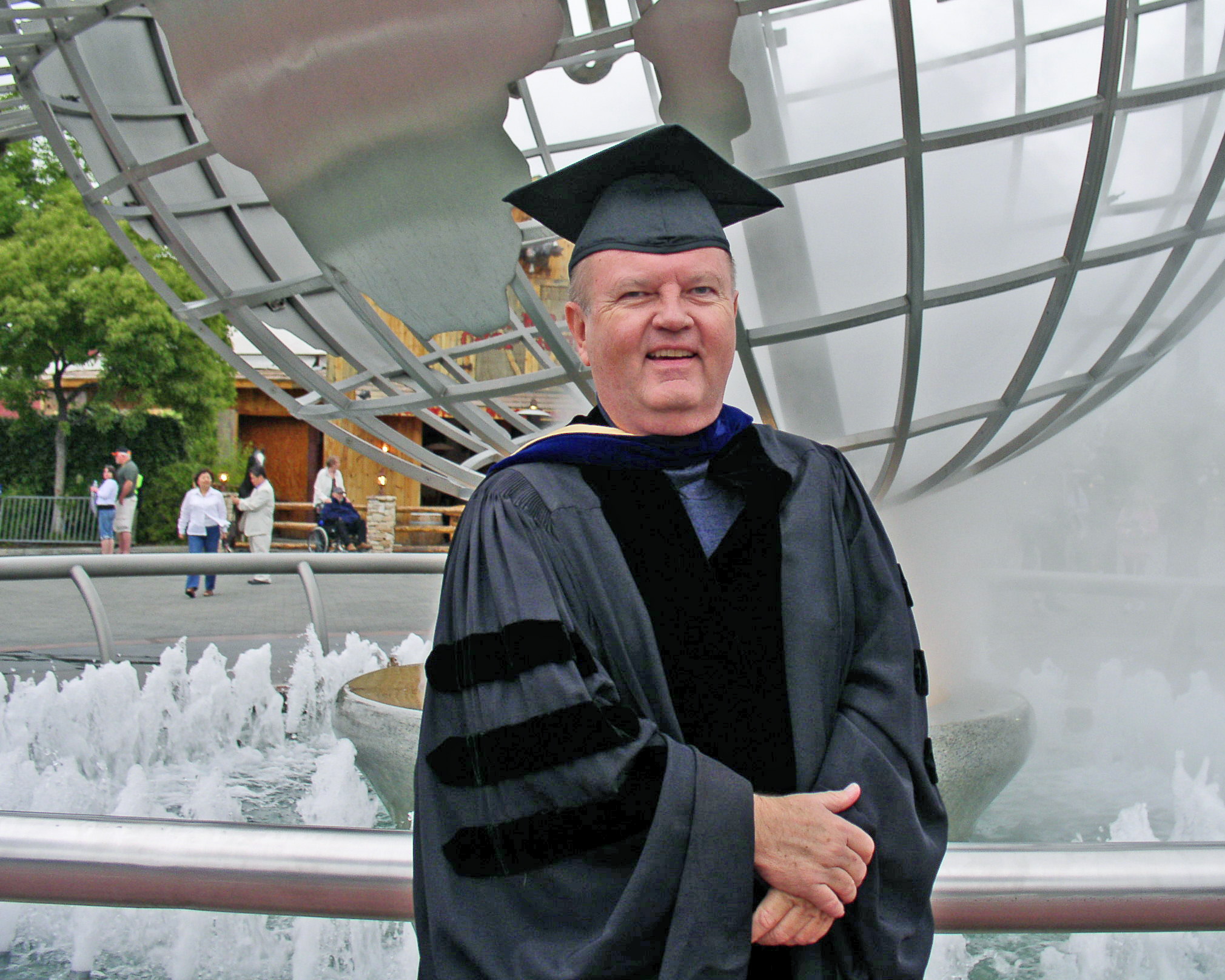 A man in graduation robes standing next to a fountain.